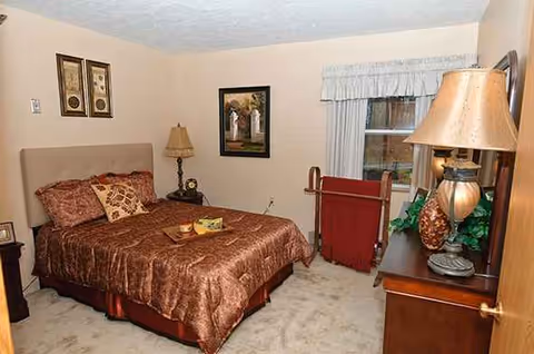 A furnished bedroom at Country Club Retirement Campus with bed, dresser, and window.