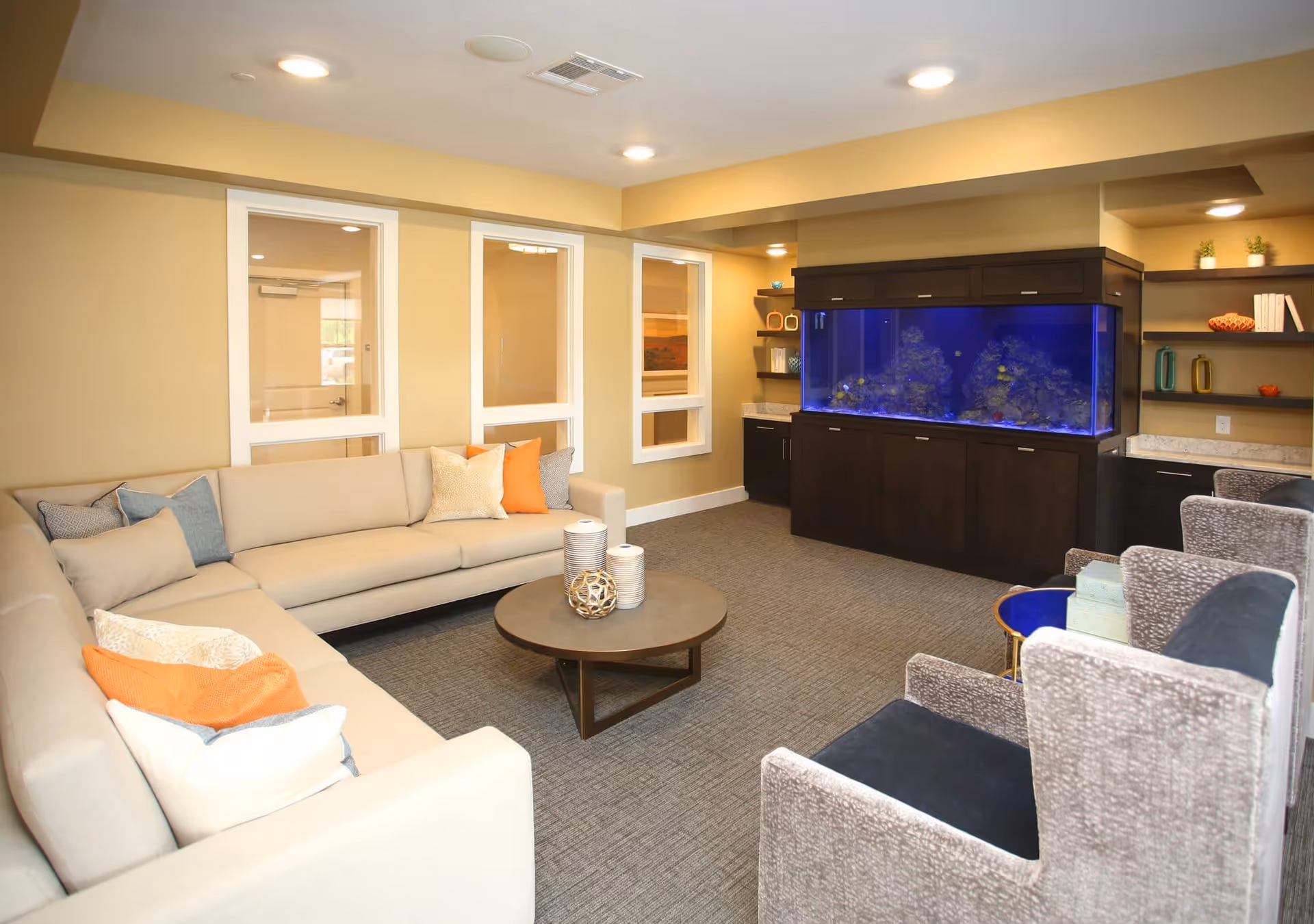 Comfortable lounge with a beige sectional sofa, armchairs, round coffee table and a large built-in aquarium.
