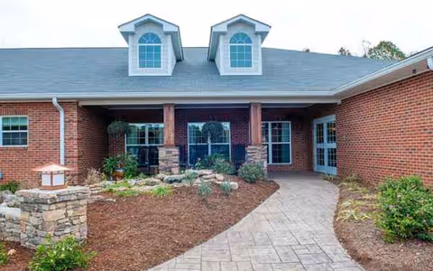 Brick senior living facility front entrance with planters and a curved walkway.