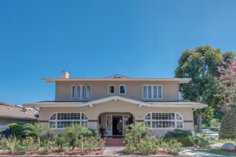 Two-story beige senior living building with arched windows and manicured front garden.