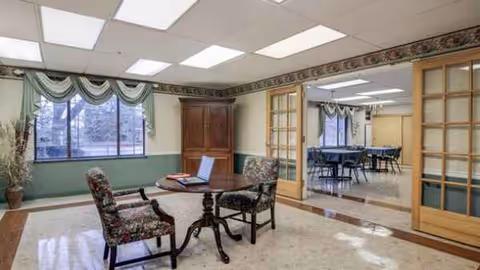 A spacious lounge area with chairs around a table and glass doors to a dining room.