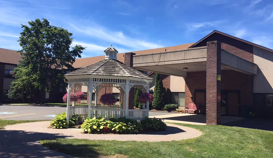 Front entrance of a senior living facility with a white gazebo, hanging flower baskets, and a covered drive-through canopy.