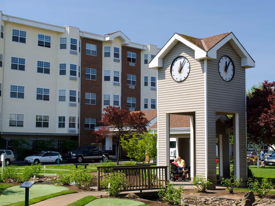 A landscaped courtyard featuring a small clock-tower pavilion in front of a multi-story apartment building.