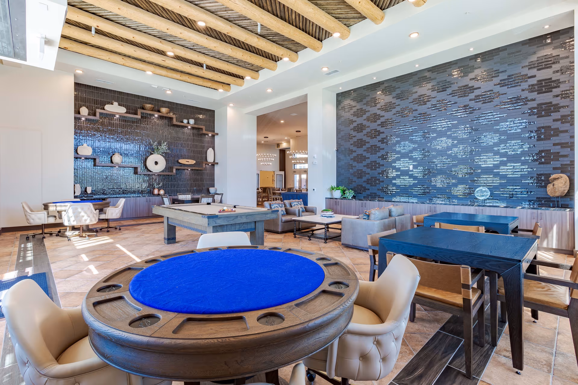 Spacious senior living common room with game and card tables, a pool table, lounge seating, decorative tiled wall, and exposed wooden ceiling beams.