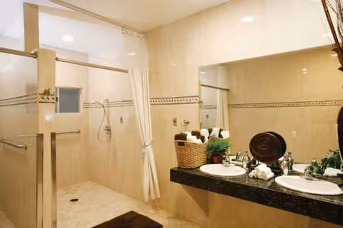 Beige-tiled bathroom with dual sinks, a shower stall, and towels.
