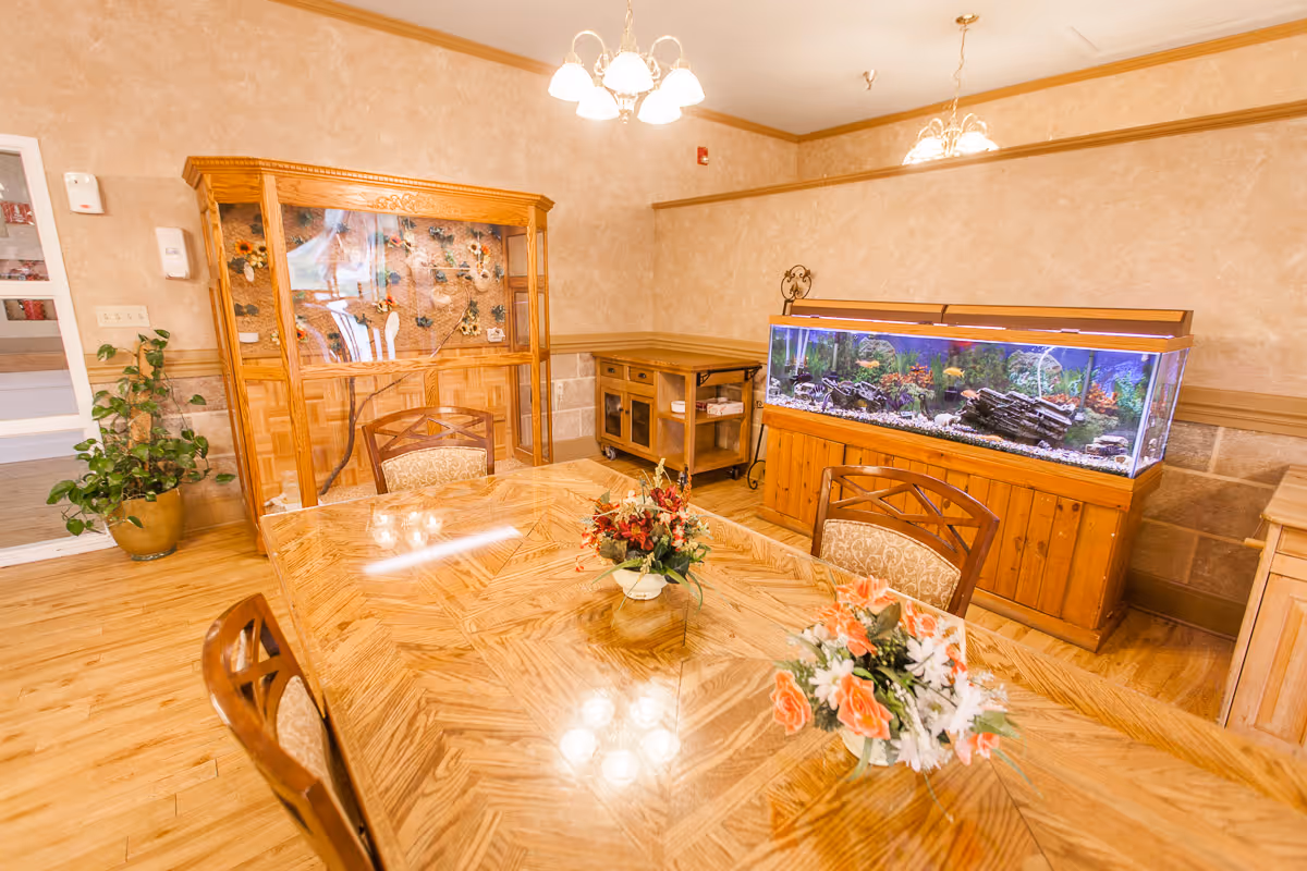 Wood-furnished communal dining room with a polished table, floral centerpieces, chairs, and a large aquarium along the wall.