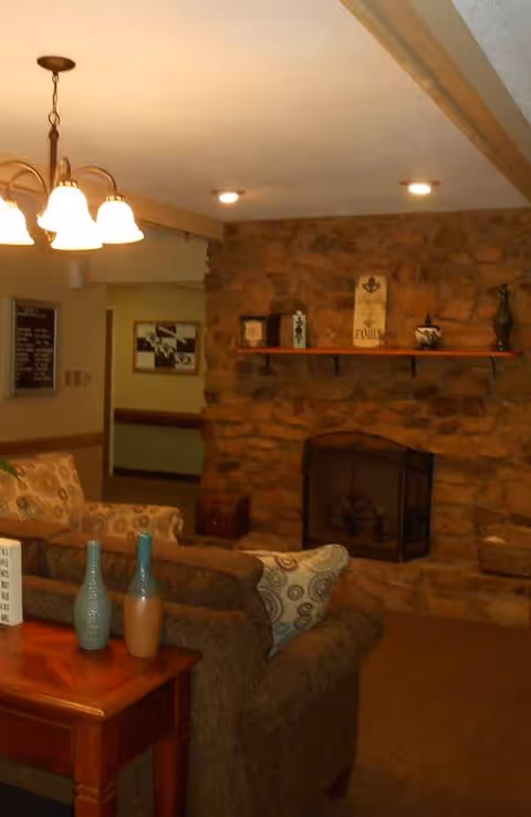 Cozy living room with stone fireplace, couches, and coffee table in a warm common area.