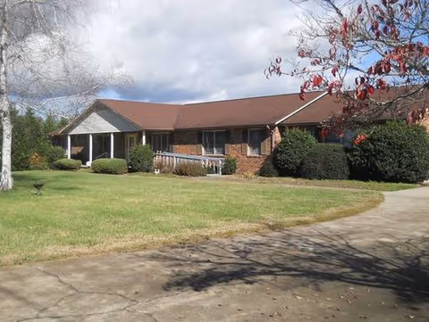 Brick, single-story care home with a front porch, lawn, and driveway.