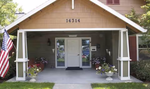 Front entrance of The Springs at Clackamas Woods with flag, address 14314, and potted plants.
