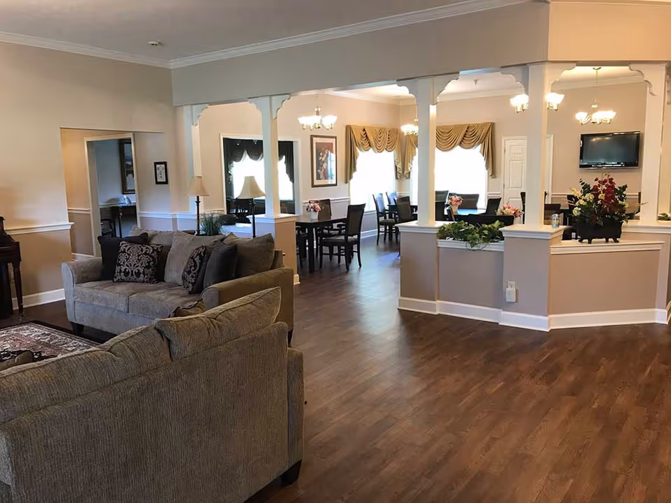 Spacious interior lounge with sofas in the foreground, dining tables and chandeliers beyond, and wood flooring.