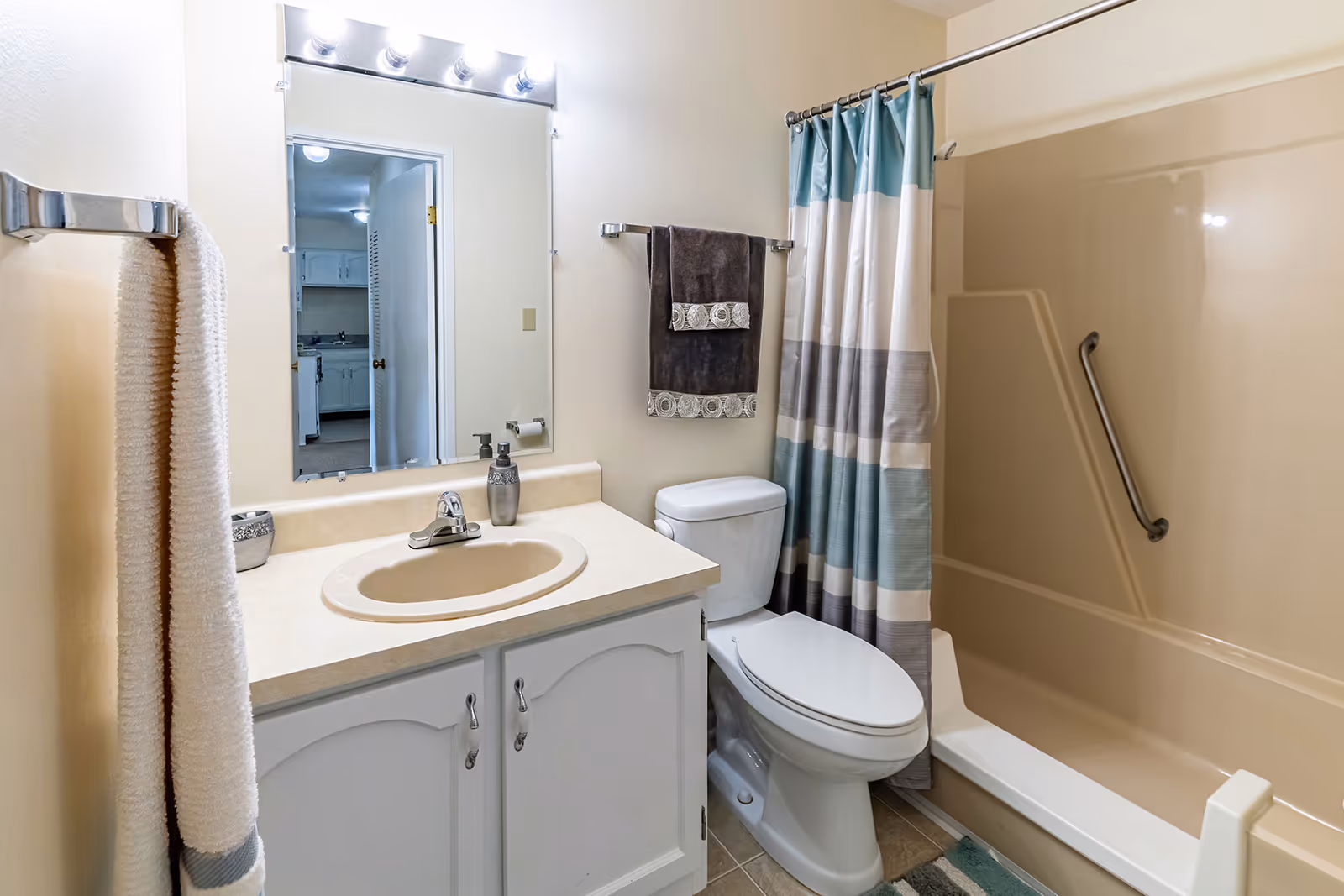 Clean bathroom with a sink vanity and mirror, toilet, and bathtub with a striped shower curtain and grab bar.