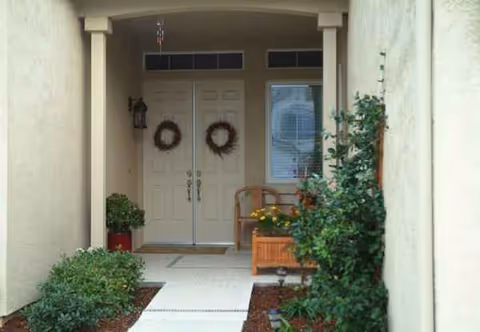 Double entry doors with wreaths, a bench, and potted plants at a covered front entrance.