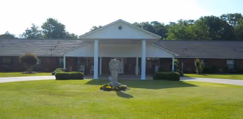 Front view of a senior living facility entrance with a statue fountain on a manicured lawn.