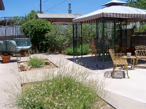 Outdoor garden patio with striped canopy, metal chairs, and potted plants.