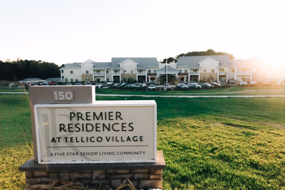 Outdoor view of Premier Residences at Tellico Village senior living community sign with the building and parking lot in the background during sunset.