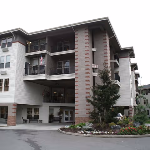 Exterior front of a multi-story senior living building with balconies, an entrance canopy, and landscaped circular driveway.