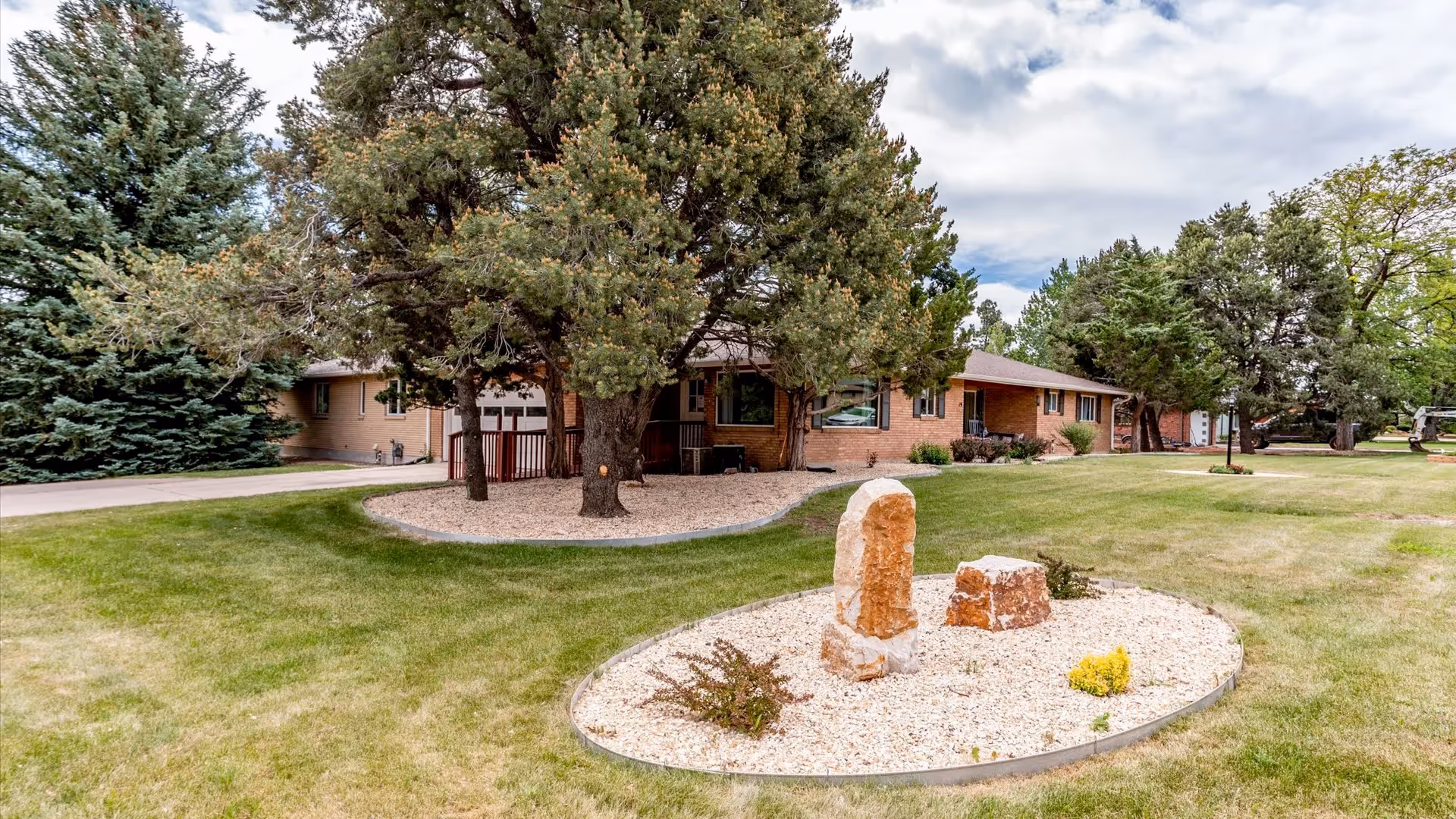Brick senior living facility with manicured lawn, trees, and circular rock garden in front.