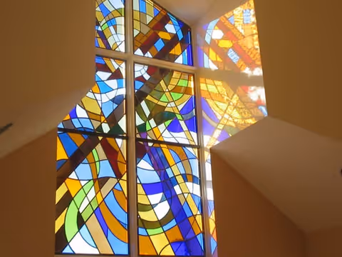 Colorful abstract stained-glass window set in a vaulted interior wall with beige surrounding surfaces.