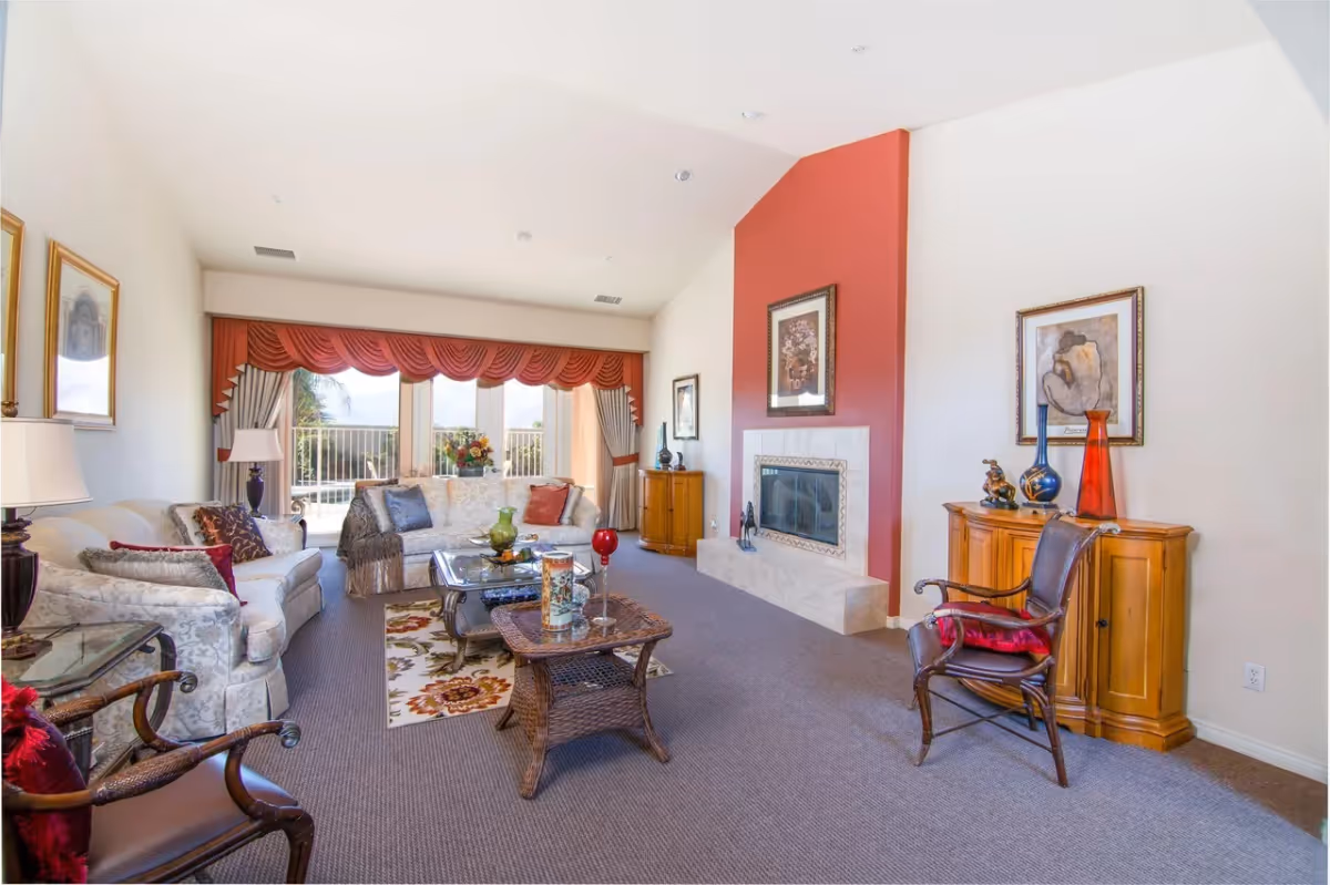 Bright, spacious living room with sofas, a wicker coffee table, a fireplace set into a red accent wall, and large windows with red valances.