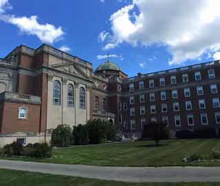 Brick senior living building with green dome, manicured lawn, and blue sky.