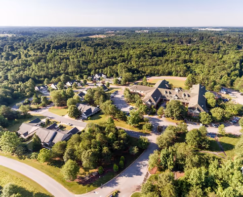 Aerial view of the Rosecrest Retirement Community campus showing a large central building, smaller residential cottages, roads and extensive surrounding trees.