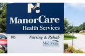 Outdoor sign for ManorCare Health Services Nursing & Rehab located at 885, with a street and trees visible in the background under a partly cloudy sky.
