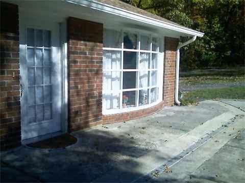 Brick exterior with curved window and white door along a concrete sidewalk.
