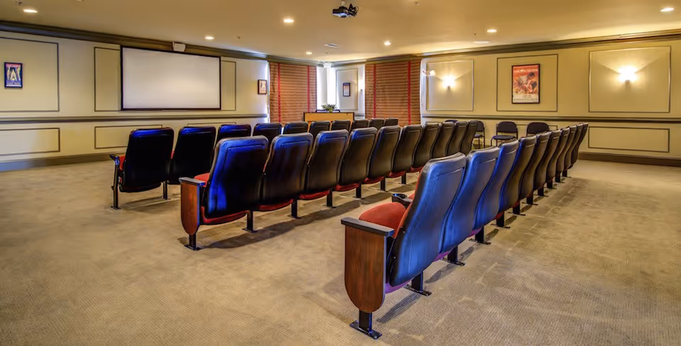 Small theater-style media room with rows of upholstered seats facing a projection screen.
