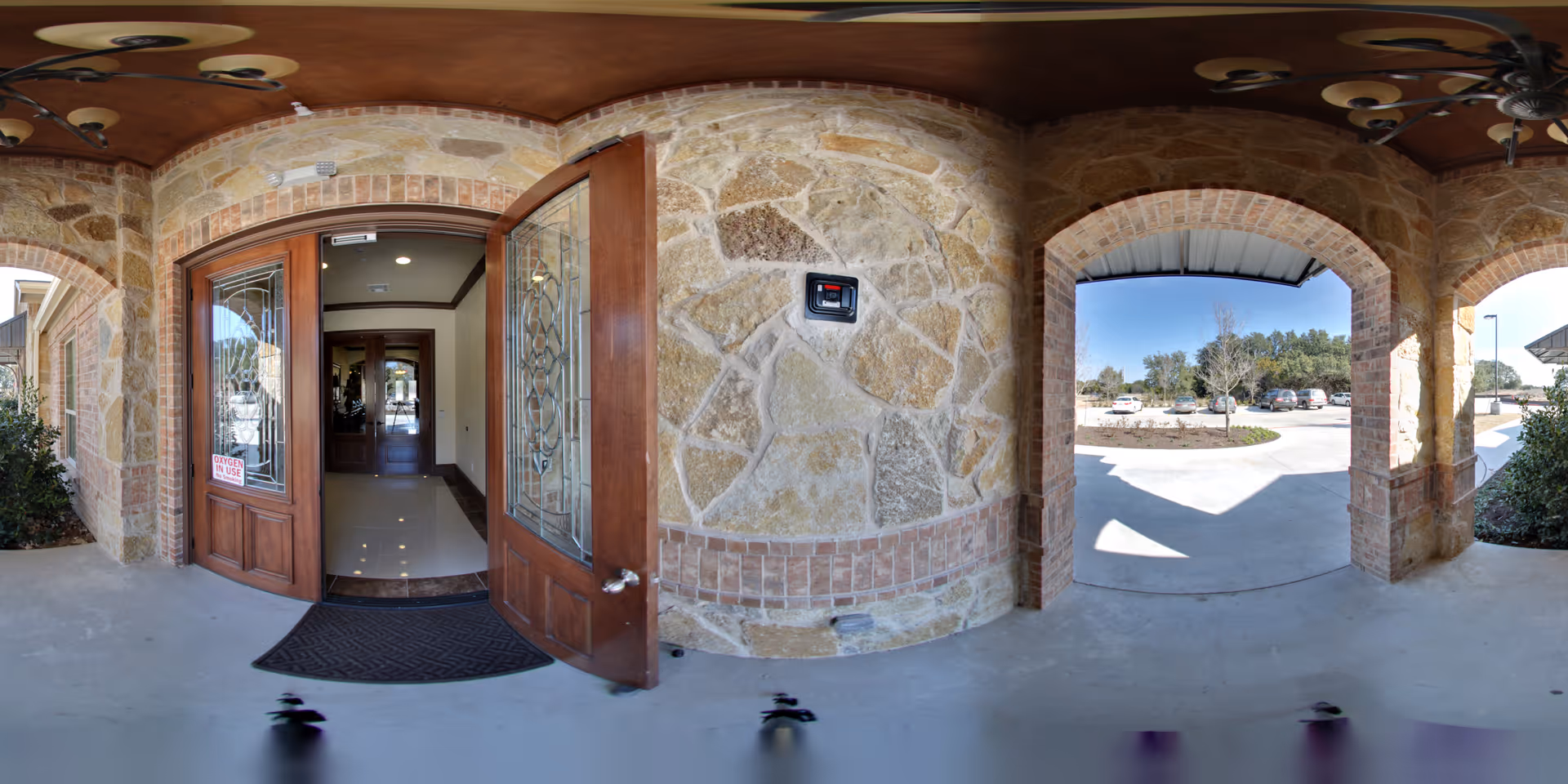 Covered stone entryway with an open wooden glass-paneled door leading into the building and arched openings to the driveway.