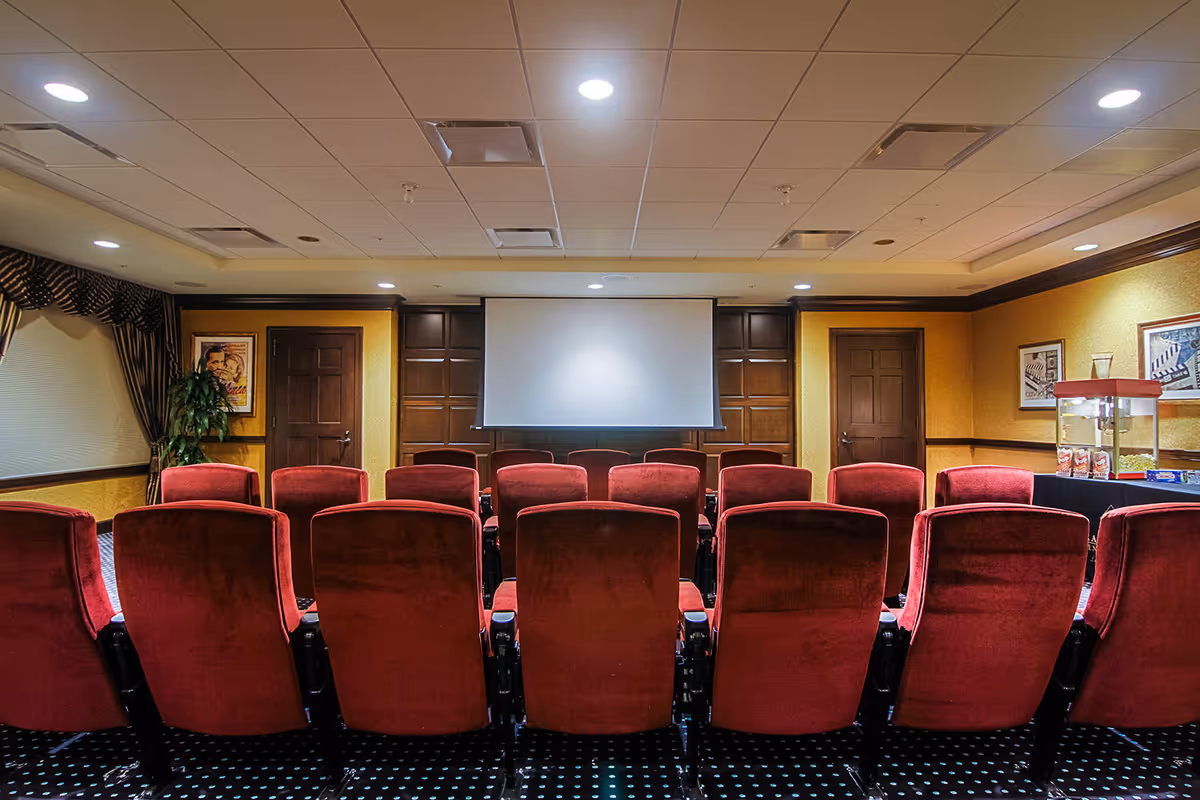 Small screening room with rows of red upholstered theater seats facing a projection screen and a popcorn machine on the right.