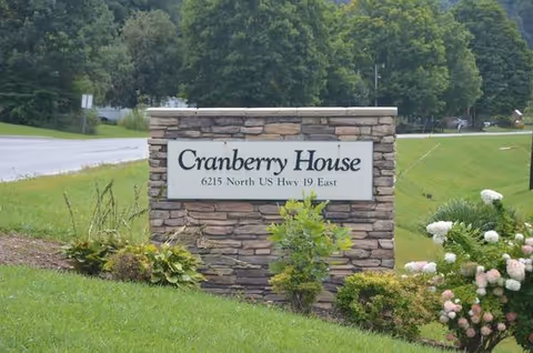 Stone Cranberry House entrance sign on a landscaped lawn with shrubs and flowers.