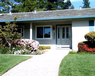 Front exterior of a single-story senior living facility with a walkway and landscaped lawn.