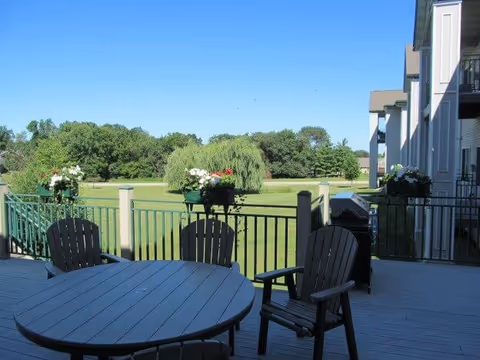Wooden patio with a round table, chairs and flower boxes overlooking a green lawn and trees.