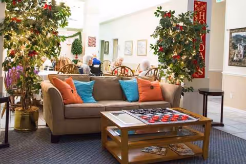 Cozy lounge with a sofa, colorful cushions, coffee table, and residents in background.