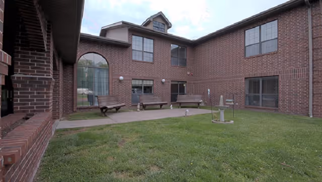 Brick two-story courtyard with benches and a small fountain on a grassy lawn.