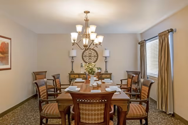 Formal dining room with a wooden table set with place settings, upholstered chairs, a chandelier overhead and a sideboard against the far wall.