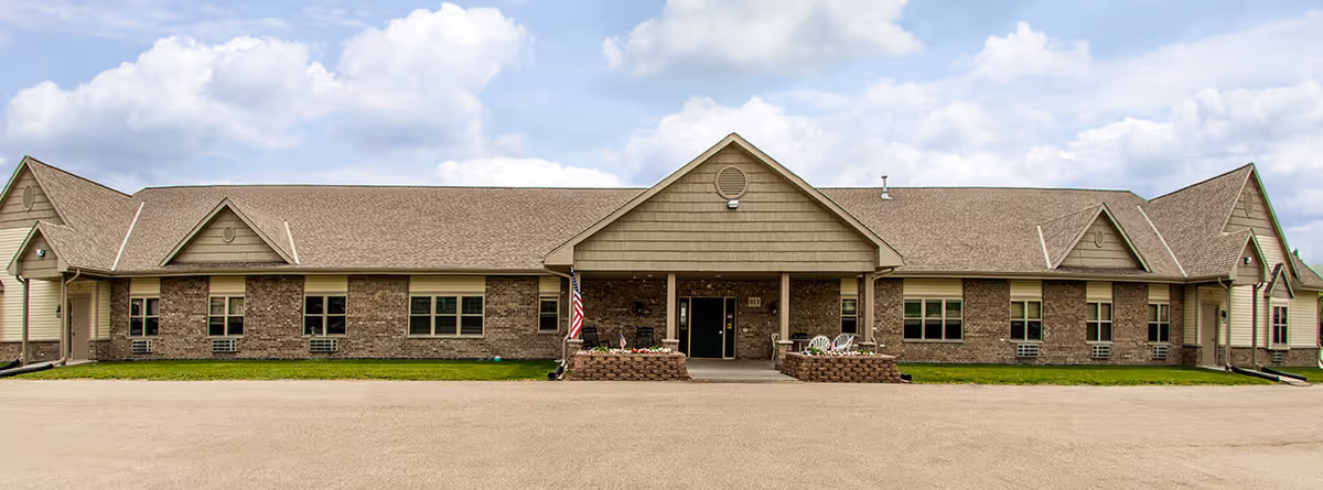 Single-story brick senior living facility building front with a central covered entrance, multiple windows, and an American flag.