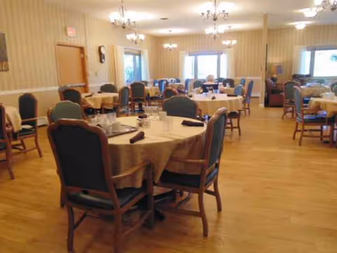 A spacious dining room with round tables, chairs, beige walls, and chandeliers.