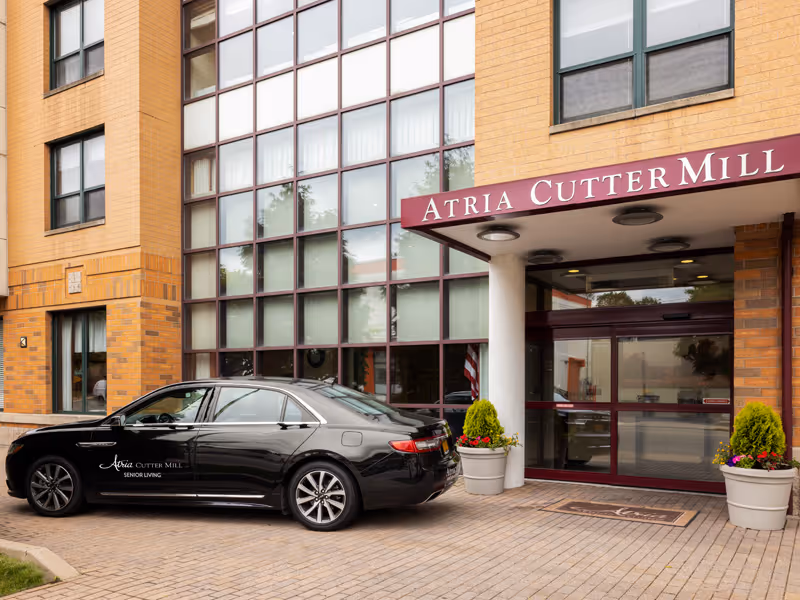 Front entrance of the Atria Cutter Mill senior living facility with a black sedan parked under the awning.