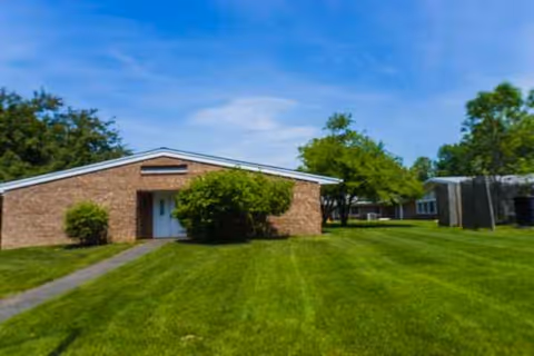 Front exterior of a brick senior care center with a well-kept green lawn.