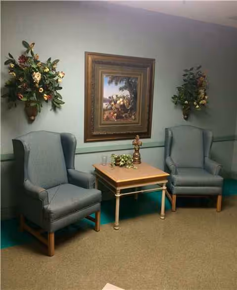 Two blue armchairs flank a small table with a plant in a pastel-walled lounge.