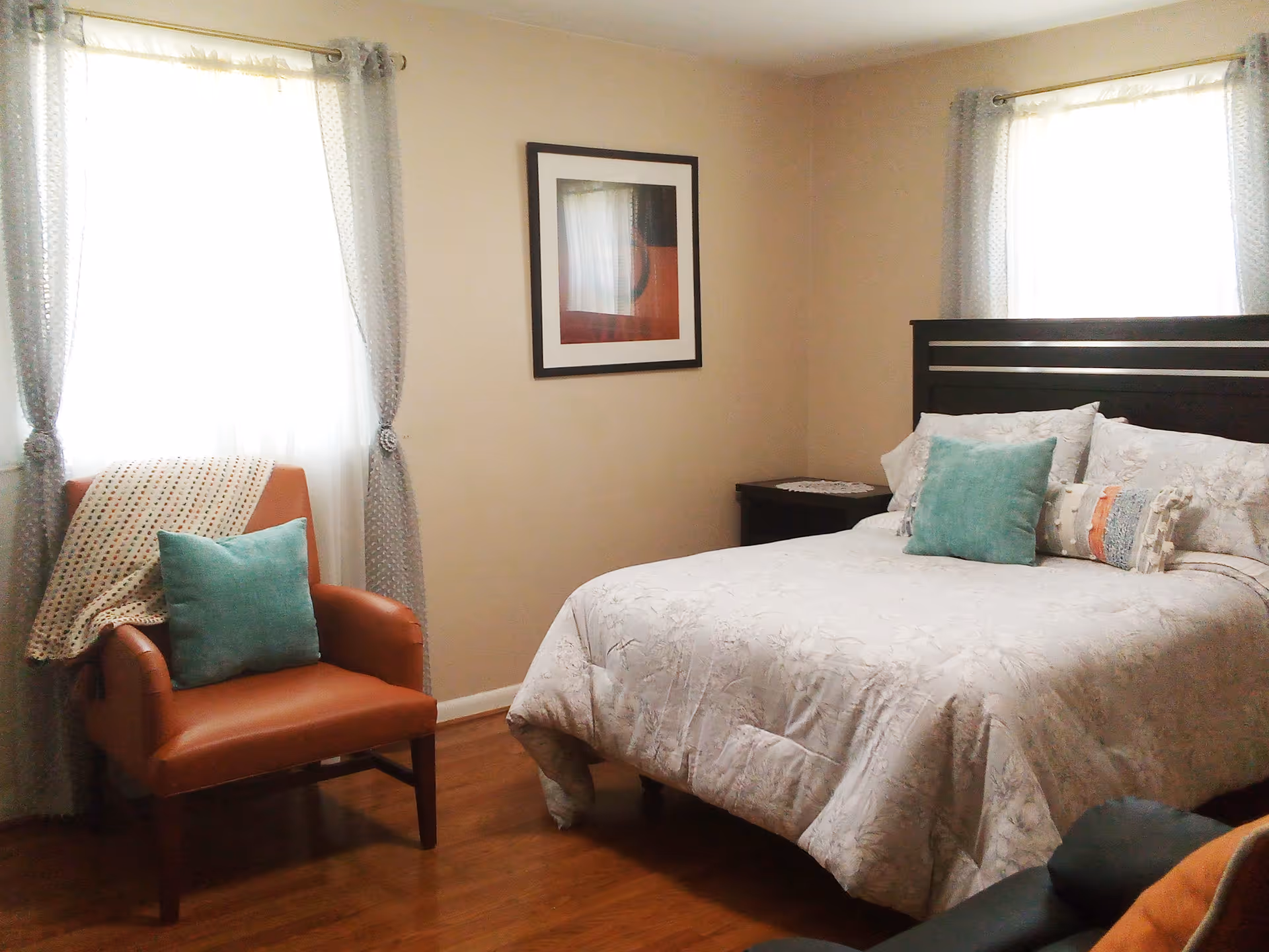 A neatly made bedroom with a bed, chair, and soft blue accents.