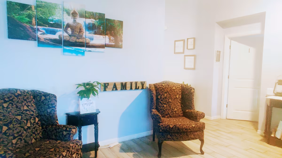 Two patterned armchairs flank a small table beneath wall art and a decorative 'FAMILY' sign in a bright sitting area.