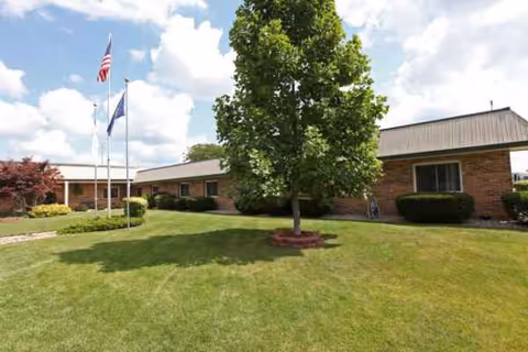 Laurels of Coldwater senior living building with manicured lawn, tree, shrubs, and flagpoles.
