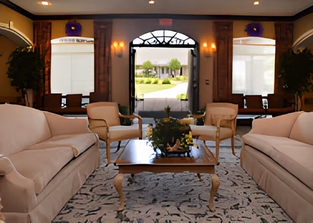 Lobby-style living room with sofas and armchairs arranged around a coffee table facing an open front door showing a landscaped walkway.