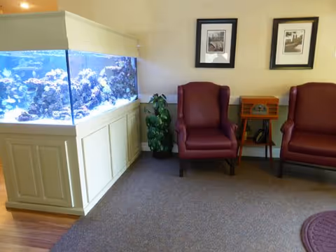 Lobby-style seating area with a large built-in aquarium to the left, two red armchairs, a small side table and framed pictures on the wall.
