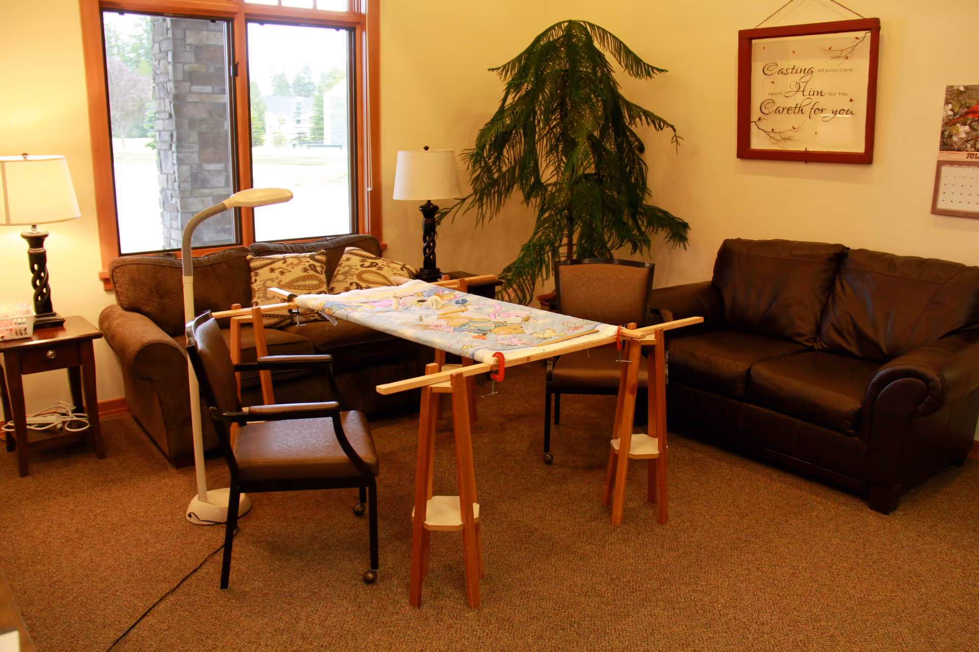 A cozy living room with sofas, chairs, lamps and a quilting frame set up on wooden sawhorses.