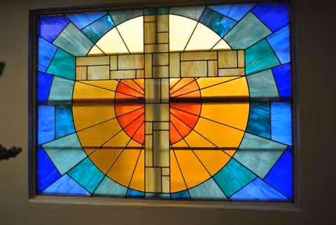 Colorful stained glass window with a cross motif and circular sunburst design.