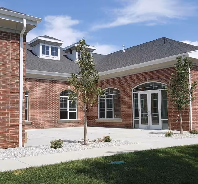 Brick senior living facility exterior with glass doors and landscaped walkway.