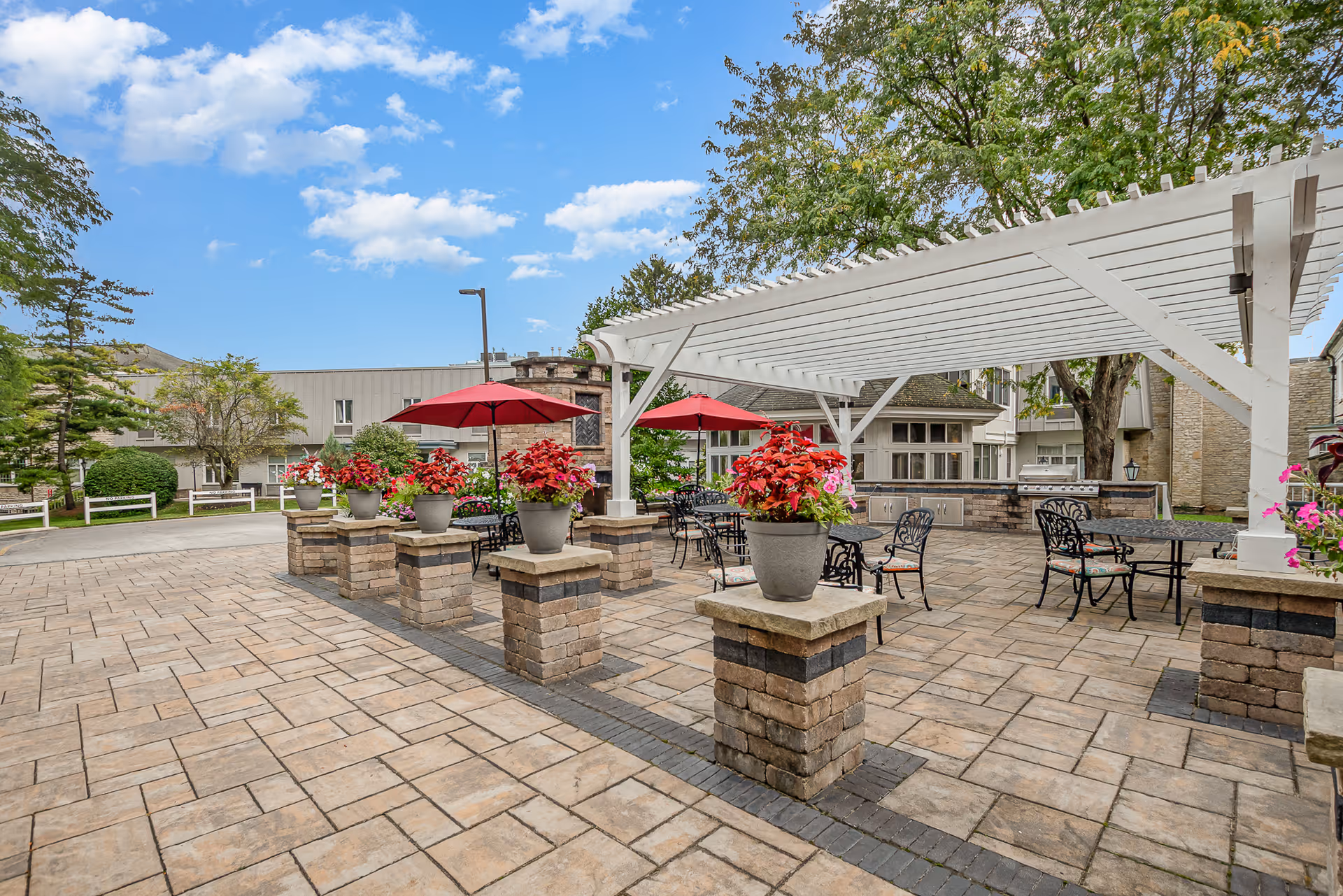 Outdoor courtyard patio with a white pergola, potted flowers, red umbrellas, and metal patio tables.